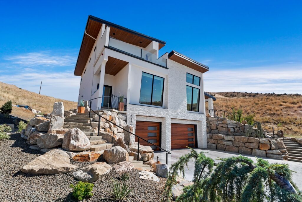 A modern home with a large garage, stone steps, and glass elements.


