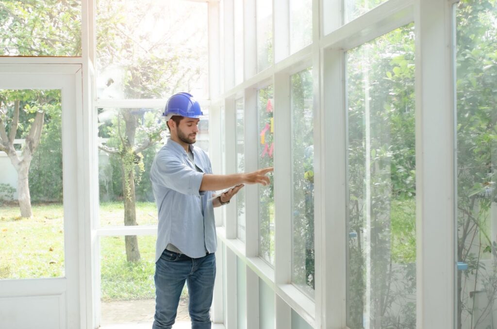 A man in a hard hat and blue shirt standing in front of large glass doors, possibly inspecting glass maintenance